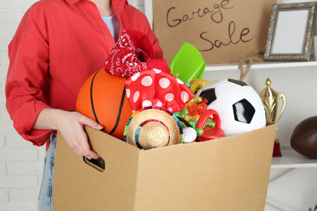 Woman holding box of unwanted stuff indoors, closeup
