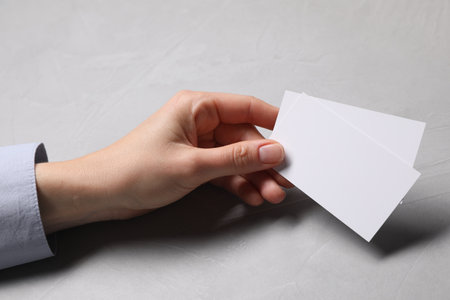 Woman holding blank cards at light gray table, closeup. Mockup for designの写真素材