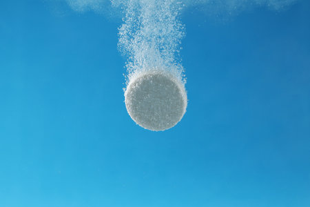 Effervescent pill dissolving in water on light blue background, closeupの写真素材