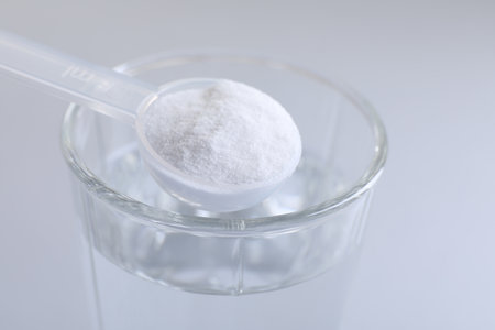 Spoon with baking soda over glass of water on light gray background, closeup