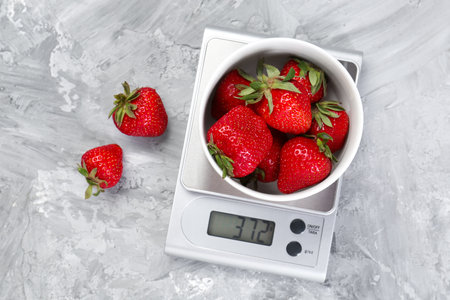 Kitchen scale with bowl of strawberries on gray textured table, flat layの写真素材