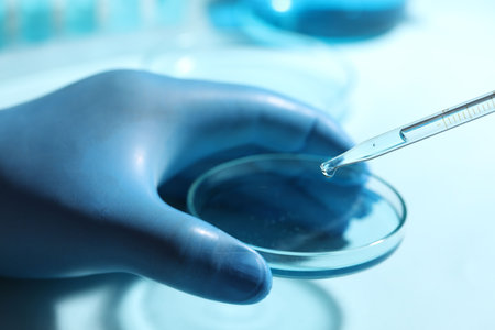Doctor dripping liquid from pipette into petri dish on blurred background, closeup. Laboratory analysisの写真素材