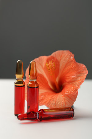 Skincare ampoules and hibiscus flower on white tableの写真素材