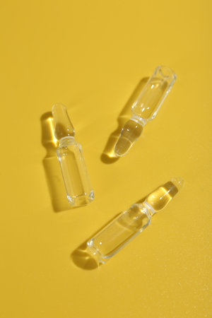 Glass ampoules with liquid on yellow background, flat layの写真素材