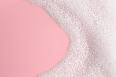 White fluffy foam on pink background, top view. Space for text