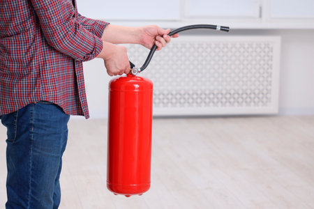 Man with fire extinguisher indoors, closeup. Space for textの写真素材