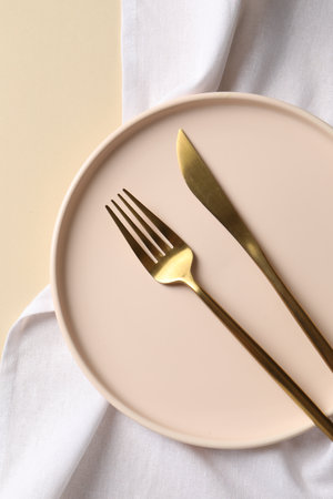 Stylish golden cutlery, plate and napkin on beige background, top viewの写真素材