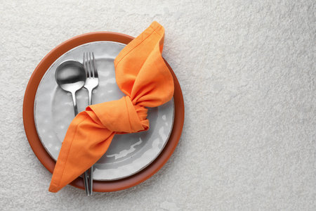 Stylish setting with cutlery, napkin and plates on light textured table, top view. Space for textの写真素材
