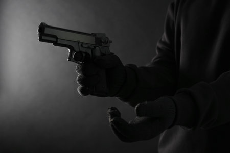 Dangerous criminal with gun on black background, closeup. Armed robberyの写真素材
