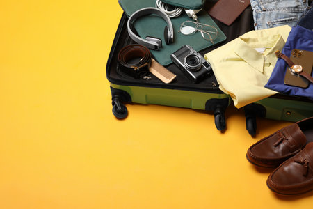Open suitcase with traveler's belongings on yellow background, space for textの写真素材