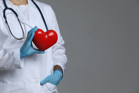 Doctor with red heart on grey background, closeup. Space for textの写真素材