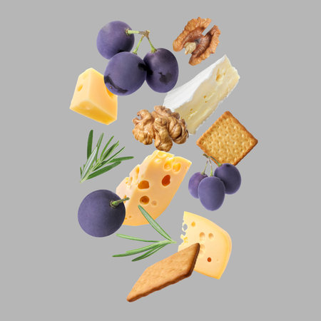 Different types of cheese, crackers, grapes, rosemary and walnut in air on grey backgroundの写真素材