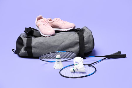 Feather badminton shuttlecocks, rackets, bag and sneakers on violet background