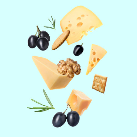 Different types of cheese, crackers, grapes, rosemary and walnut in air on light blue backgroundの写真素材
