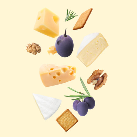 Different types of cheese, crackers, grapes, rosemary and walnuts in air on beige backgroundの写真素材