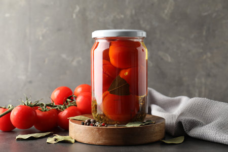 Tasty pickled tomatoes in jar, spices and fresh vegetables on gray tableの写真素材