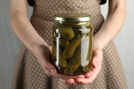 Woman holding jar with pickled cucumbers on gray background, closeupの写真素材