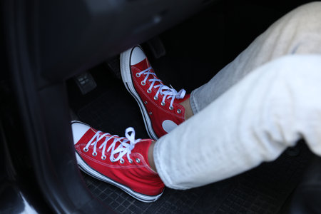 Woman in sneakers pushing on pedal of car brake, closeup