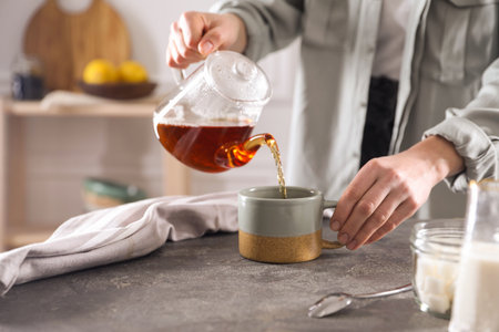 Woman pouring hot tea into cup at gray table, closeupの写真素材
