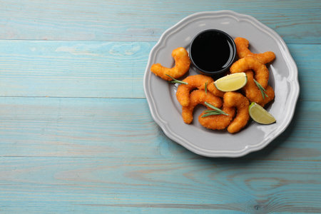 Delicious breaded fried shrimps, lime, rosemary and sauce on light blue wooden table, top view....