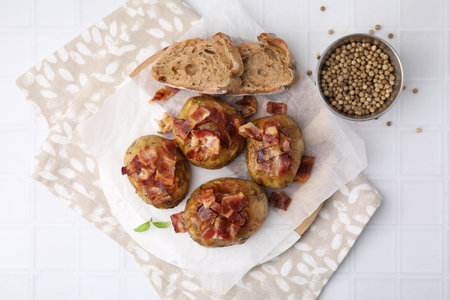 Delicious baked potatoes with bacon, bread and peppercorns on white tiled table, flat layの写真素材