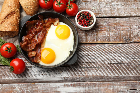 Tasty bacon and eggs in dish among products on wooden table, flat lay. Space for textの写真素材