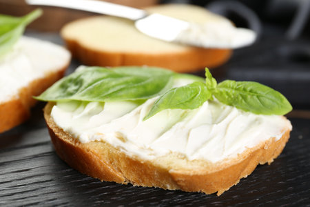 Piece of bread with cream cheese and basil on black wooden table, closeupの写真素材