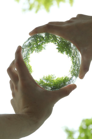 Overturned reflection of beautiful green trees outdoors, low angle view. Man holding crystal ball in park, closeupの写真素材
