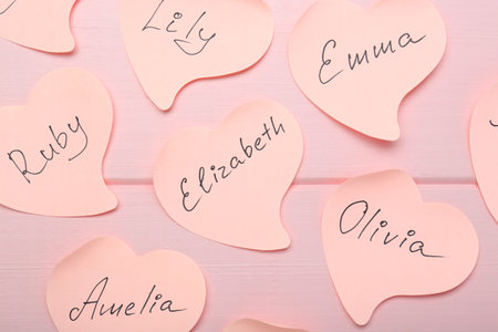 Paper stickers with different names on pink wooden background, flat lay. Choosing baby's nameの写真素材