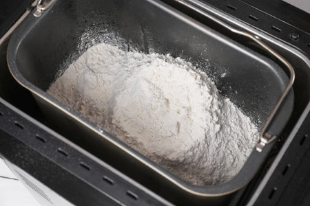 Modern breadmaker with flour on table, closeup