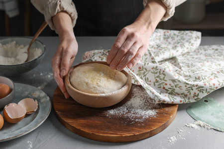 Woman covering dough with napkin at gray table, closeupの写真素材