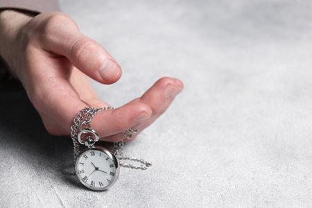 Man holding chain with elegant pocket watch at gray textured table, closeup. Space for text