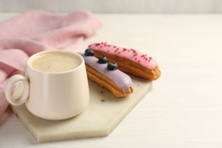 Cup of coffee and delicious eclairs covered with glaze on white wooden table. Space for text