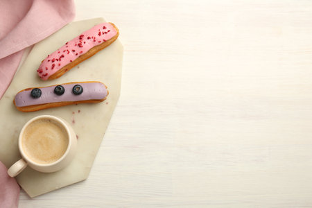 Cup of coffee and delicious eclairs covered with glaze on white wooden table, top view. Space for textの写真素材