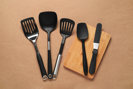 Different spatulas on brown background, flat lay