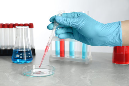 Scientist dripping liquid from pipette into petri dish at gray marble table, closeup