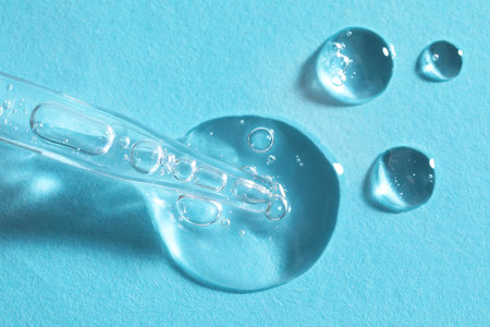 Glass pipette and transparent liquid on light blue background, top viewの写真素材