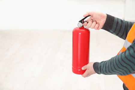 Man with fire extinguisher indoors, closeup. Space for textの写真素材