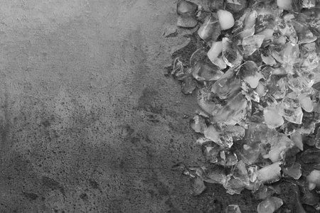 Pieces of crushed ice on dark textured table, top view. Space for text