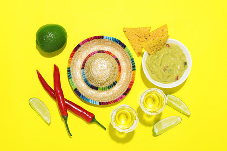Mexican sombrero hat, tequila, nachos chips, guacamole and other products on yellow background, flat...
