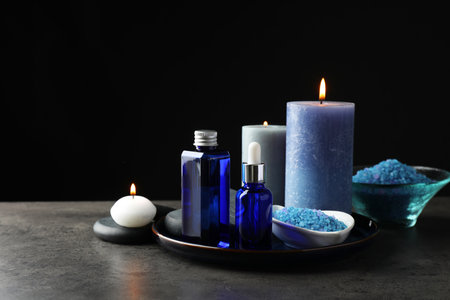 Spa composition. Cosmetic products, burning candles and sea salt on gray table against black background, space for textの写真素材
