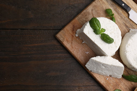 Fresh ricotta (cream cheese), basil, bread and knife on wooden table, top view. Space for textの写真素材