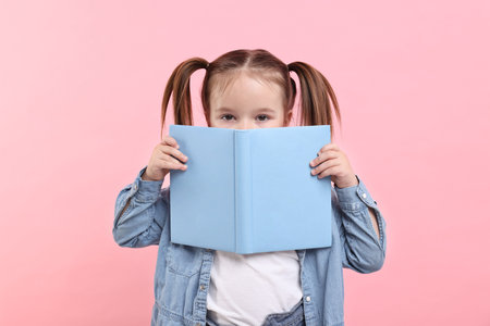 Cute little girl with open book on pink backgroundの写真素材