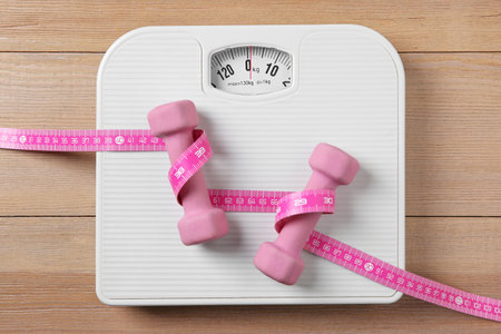 Scale, measuring tape and dumbbells on wooden floor, top viewの写真素材