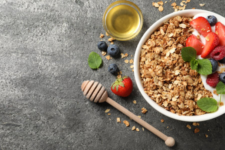 Tasty granola with berries, yogurt and honey on gray textured table, flat lay. Space for text