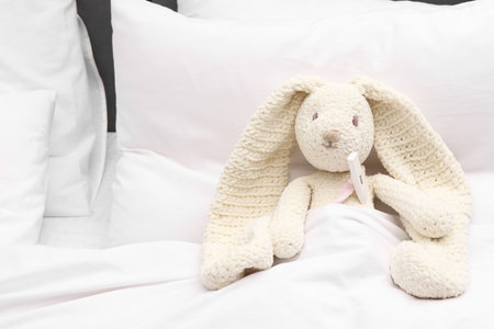 Toy cute bunny with thermometer under blanket in bedの写真素材