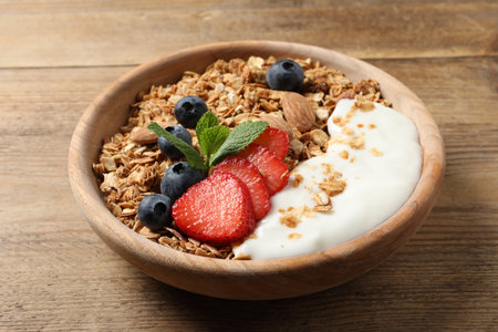 Tasty granola with berries, almond and yogurt in bowl on wooden table, closeupの写真素材