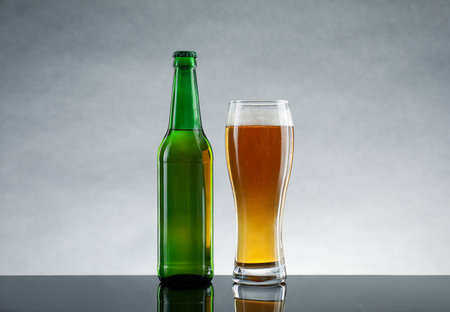Bottle and glass of beer on table against light gray backgroundの写真素材