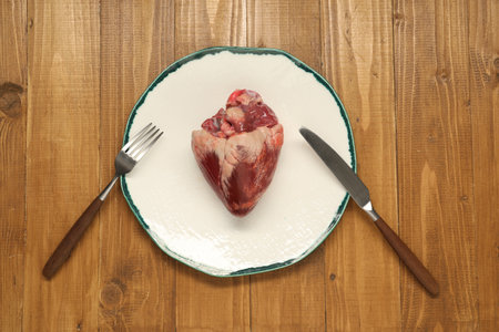 Raw heart, fork and knife on wooden table, top viewの写真素材