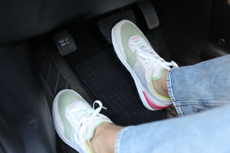 Woman in sneakers pushing on pedal of car brake, closeup